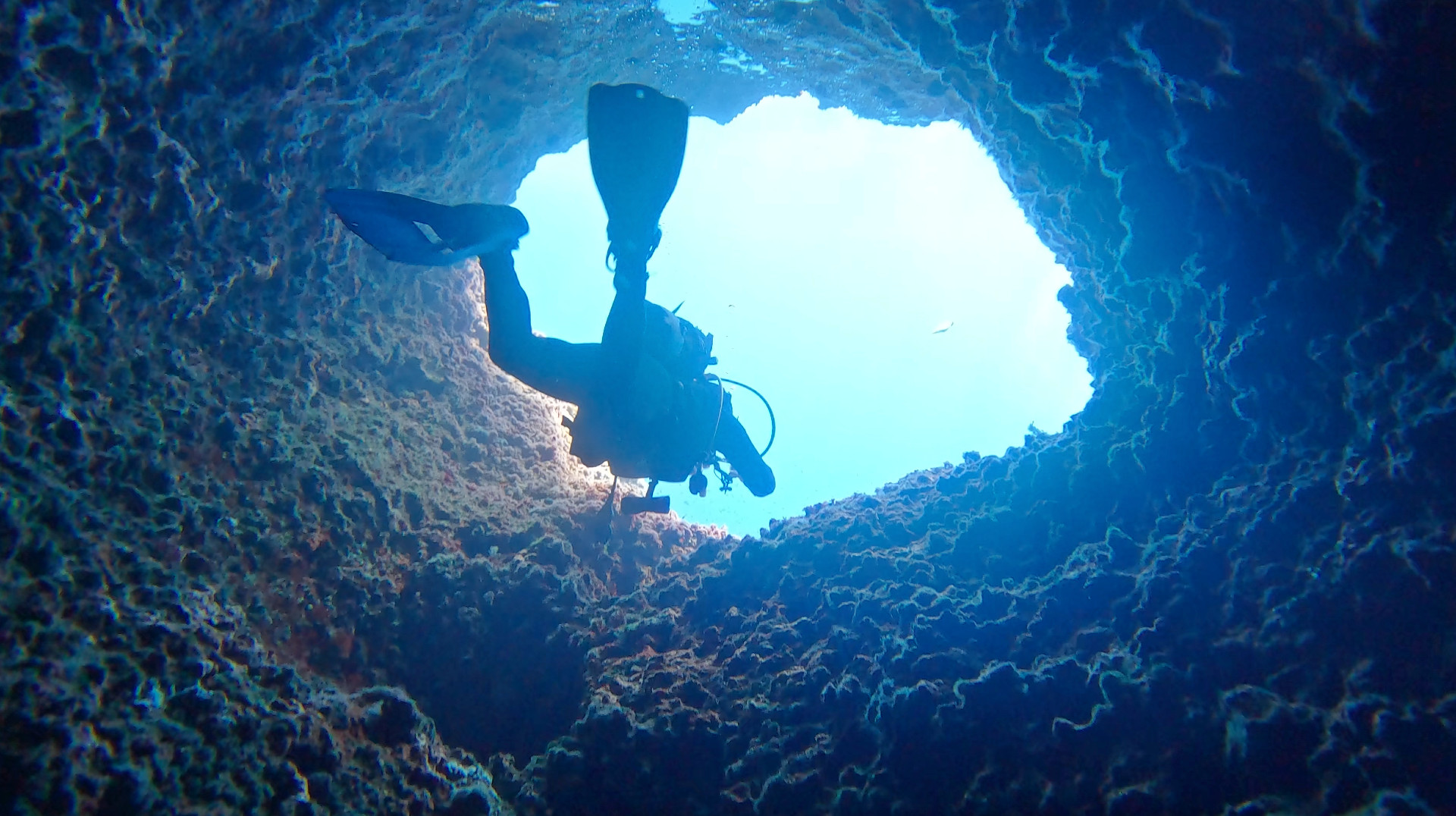 Un buceador ascendiendo por aguas cristalinas de color azul rodeado de formaciones rocosas submarinas, con una suave luz filtrándose desde la superficie, evocando una sensación de quietud y soledad apacible
